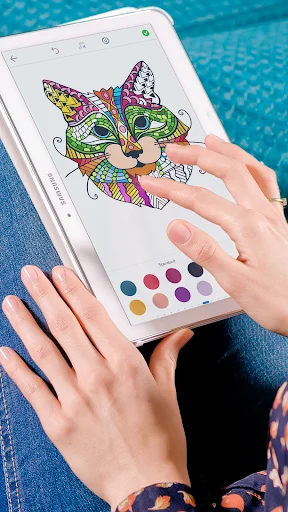 Adult user holding tablet while coloring detailed mandala cat design with stylus and multiple color options displayed