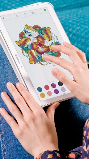 Hands holding tablet displaying interactive mandala coloring app with vibrant color palette for digital painting and relaxation